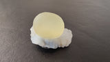 Pale yellow translucent fluorite sphere resting atop a rough white quartz matrix on a dark, smooth surface.