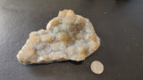 Small Brazilian amethyst druzy cluster with white and pale yellow crystal formations, shown beside a quarter for size on a black textured surface.