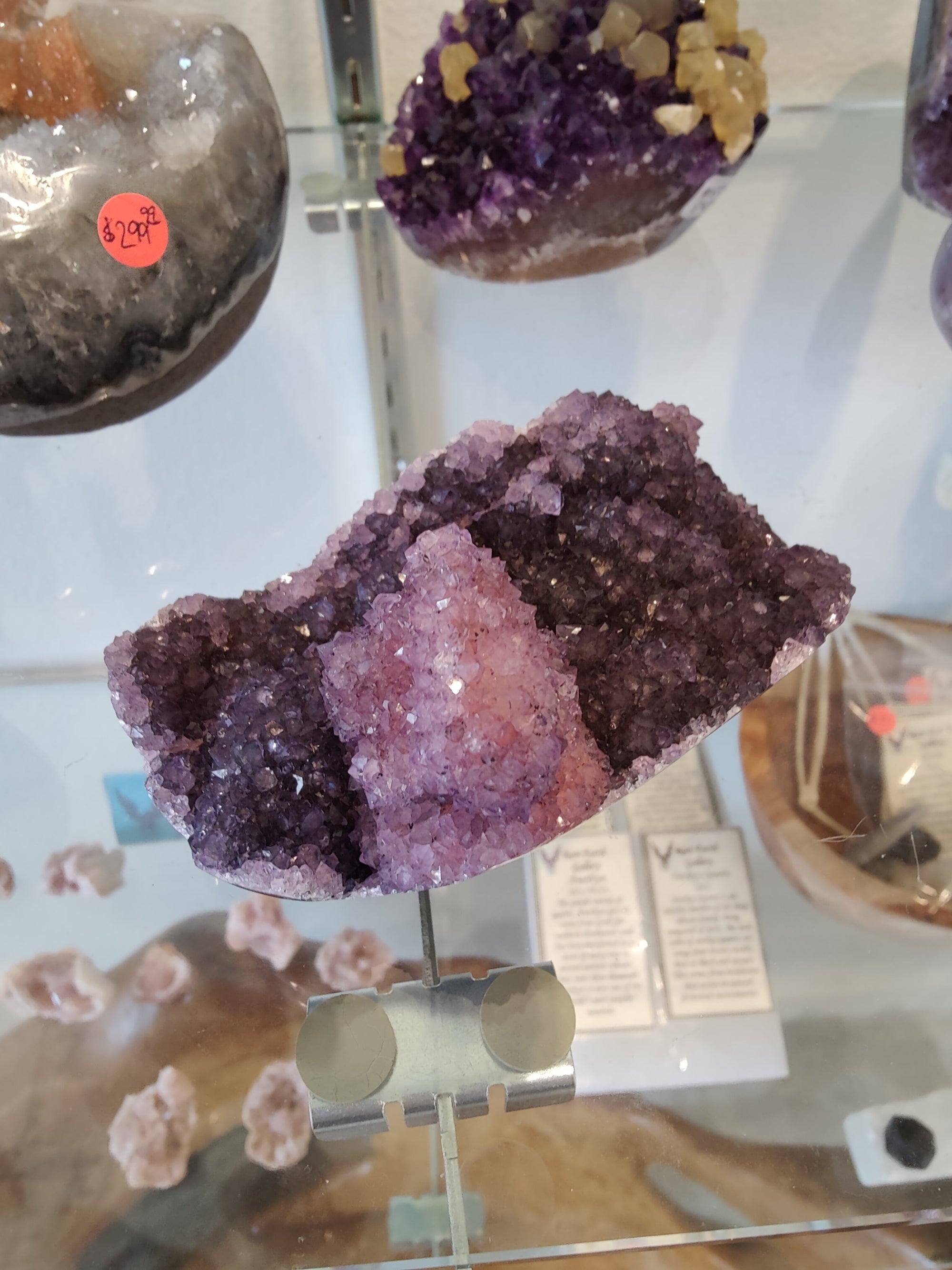Polished amethyst geode sculpture with natural purple crystals, standing on a white base.