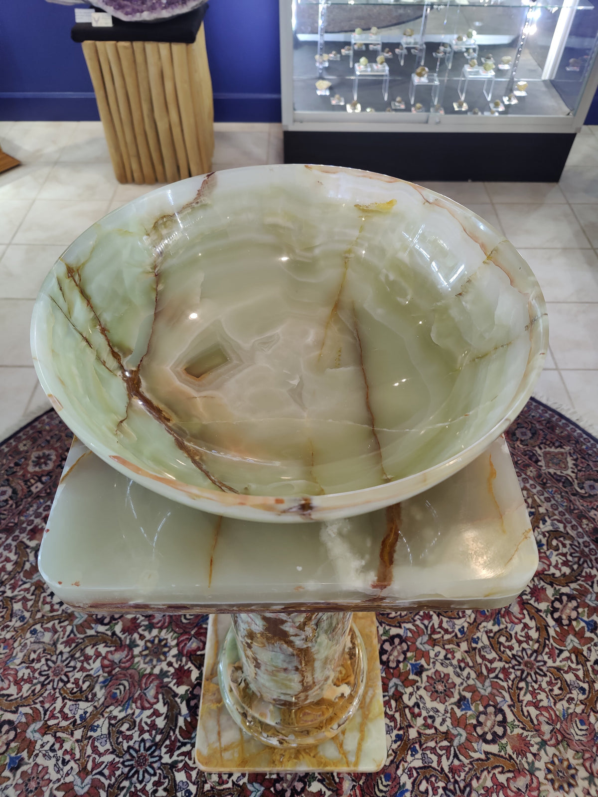 Round green onyx bowl with natural veining in shades of brown and cream, displayed on a matching square onyx pedestal with similar patterns.