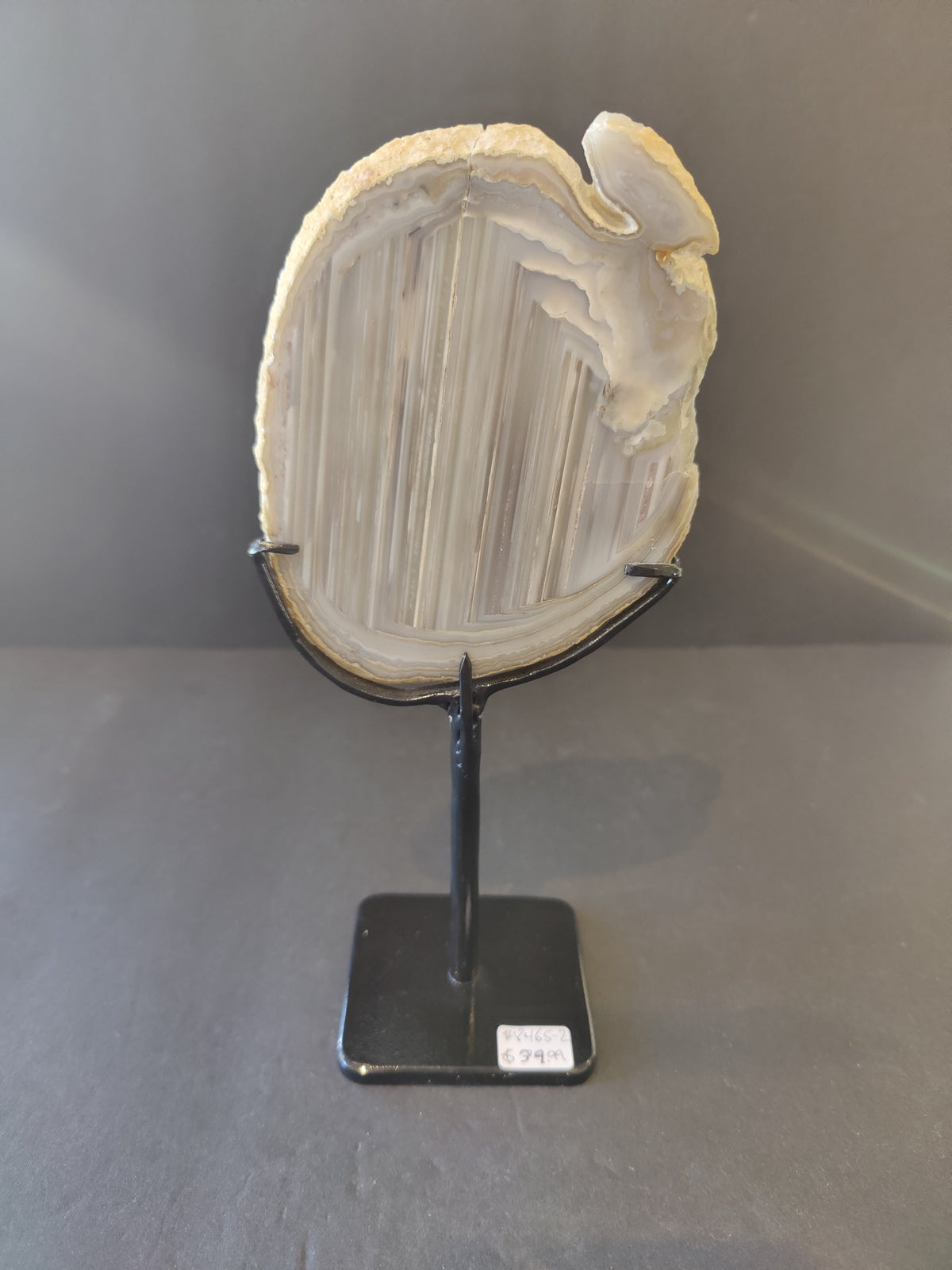 Translucent pale beige and white agate slice with natural striations mounted vertically on a black metal stand with a square base and price tag.