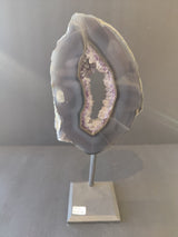 Gray and white banded agate slice with a crystalline purple center, mounted vertically on a slender metal stand with a square base.