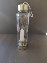 Clear glass water bottle with stainless steel lid and base containing a rose quartz crystal point inside, against a dark background.