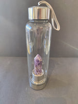 Clear glass water bottle with silver metal cap and base, containing a purple amethyst crystal point inside the base section.