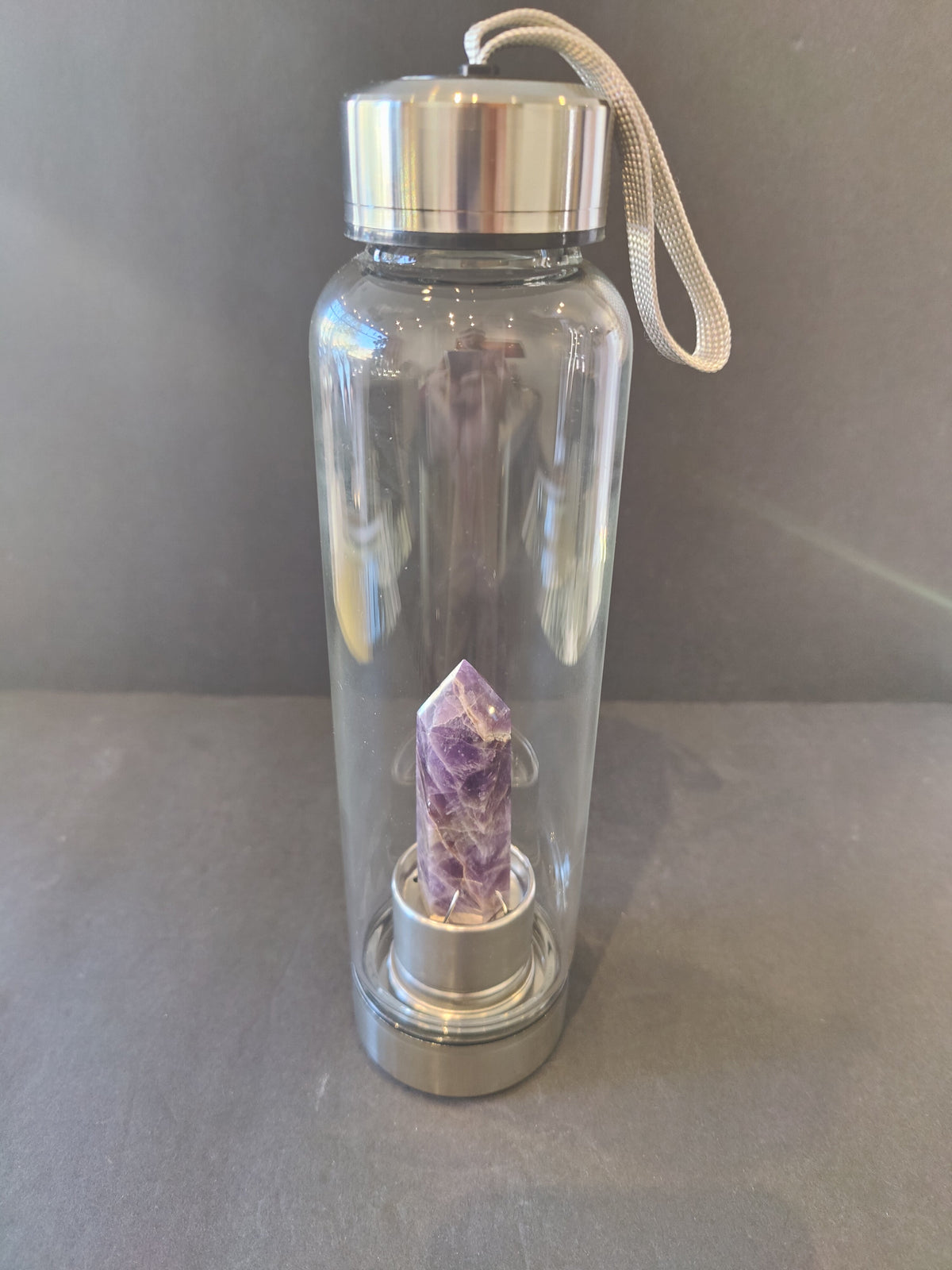 Clear glass water bottle with silver metal cap and base, containing a purple amethyst crystal point inside the base section.