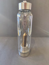 Clear glass water bottle with silver metal lid and base, containing a pointed crystal inside, standing against a plain dark background.