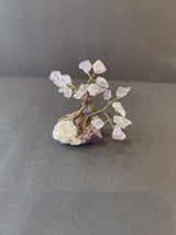 Small bonsai tree sculpture with twisted brown wire trunk and branches holding translucent purple crystal leaves on a rough purple and white rock base.