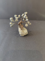 Small bonsai tree sculpture with silver crystal clusters for foliage, mounted on a textured rectangular silver crystal base, against a plain dark background.