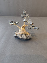 Small bonsai-style sculpture with a twisted wooden trunk mounted on a dark rock base, branches holding irregular black crystal clusters.