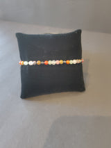 Delicate 4mm beaded stone bracelet featuring small multicolored round beads in earthy tones displayed on a black cushion against a neutral background.