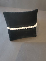 Bracelet of small, round white beads with gray marbling displayed on a black velvet cushion against a gray background.