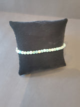 Delicate 4mm beaded bracelet with pale blue and green stones displayed on a small black cushioned pillow against a neutral background.