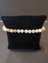 Stretch bracelet of smooth round beads in shades from white to pale orange, displayed on a black velvet pillow.
