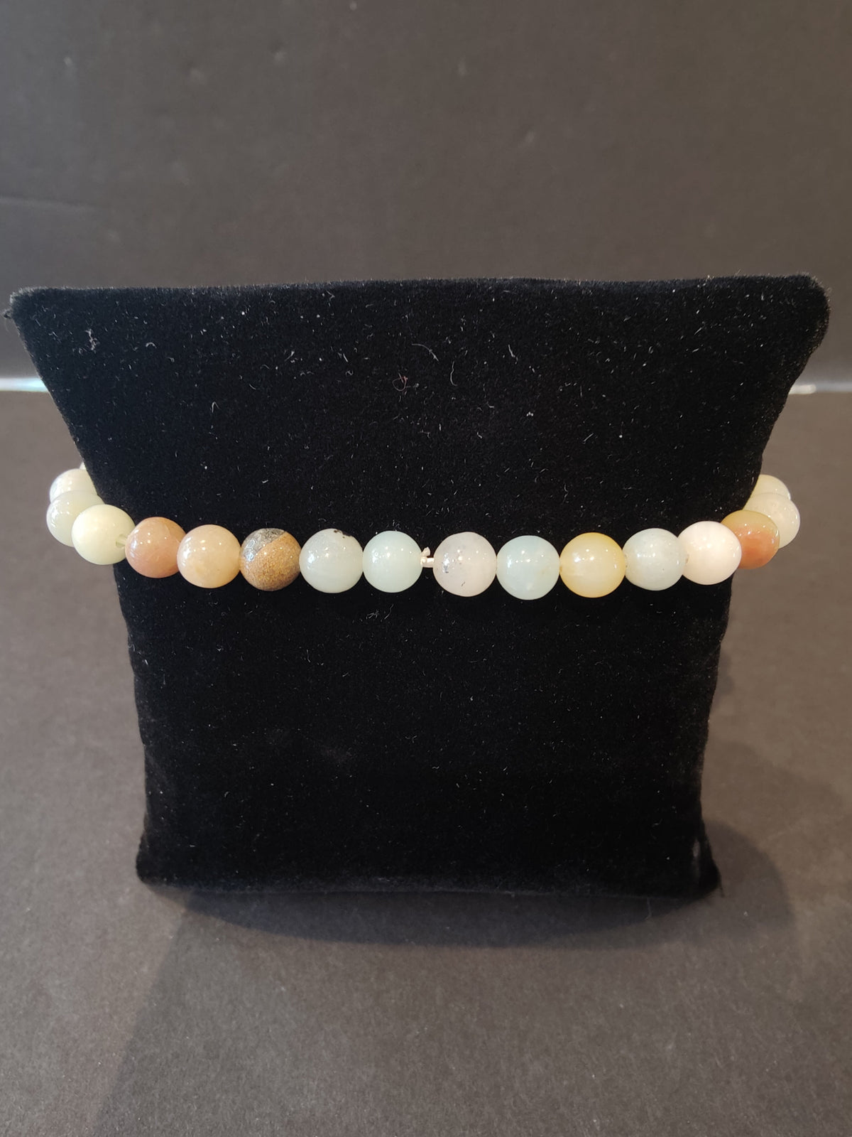Stretch bracelet of smooth round beads in shades from white to pale orange, displayed on a black velvet pillow.