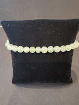 Single-strand bracelet of translucent pale green 6mm round stone beads displayed on a black velvety cushion against a neutral background.
