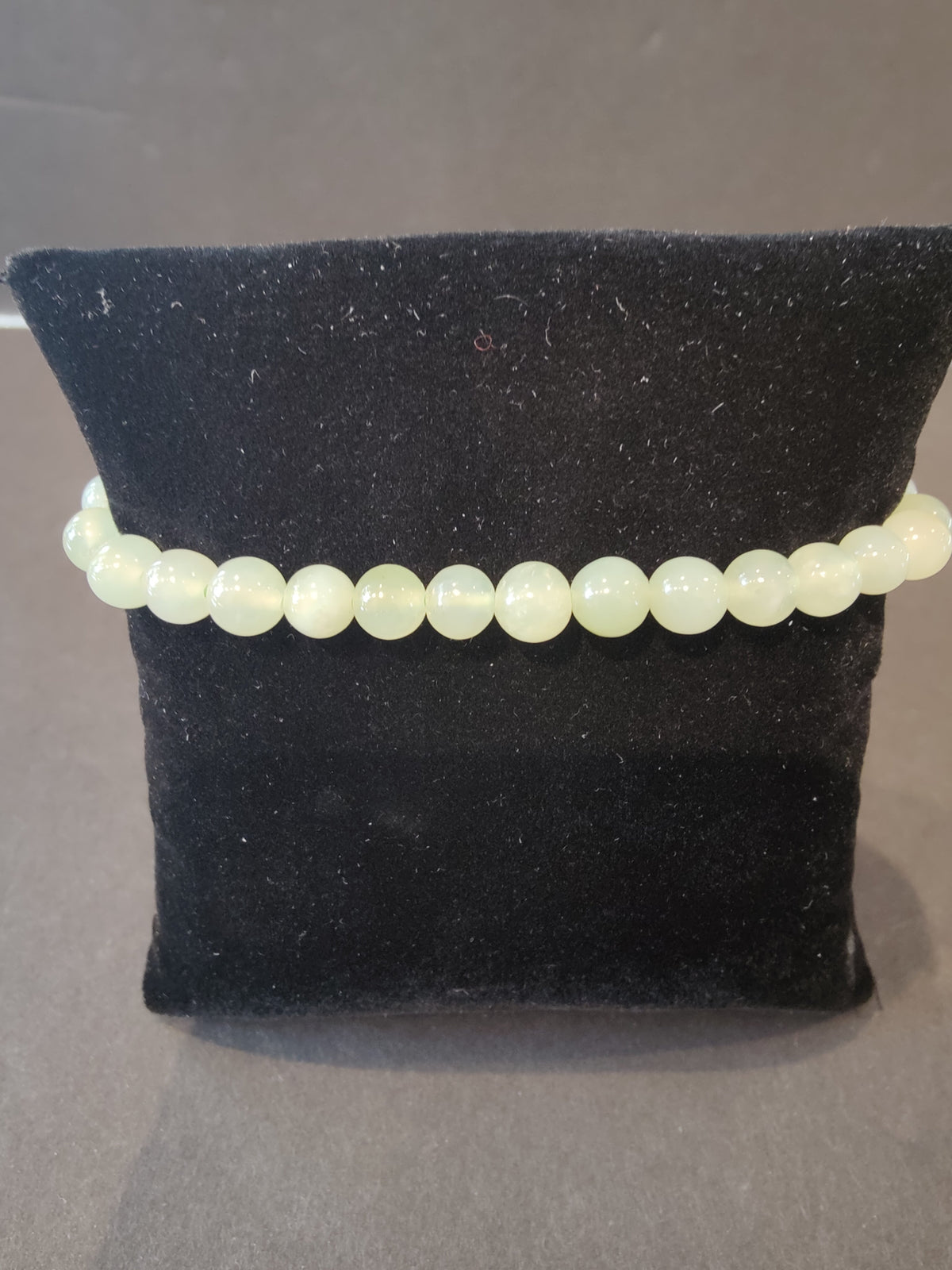 Single-strand bracelet of translucent pale green 6mm round stone beads displayed on a black velvety cushion against a neutral background.
