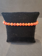 Round 6mm orange stone bead bracelet displayed on a black cushioned stand against a neutral background.