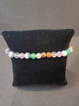 Bracelet of 6mm multicolored stone beads including purple, green, orange, white, and clear, displayed on a black fabric cushion.