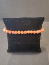 Bracelet of round 6mm reddish-orange beaded stones with a subtle sparkling texture displayed on a small black velvet pillow.