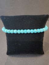 Turquoise-colored beaded stone bracelet with smooth 6mm round beads displayed on a small black velvet cushion.