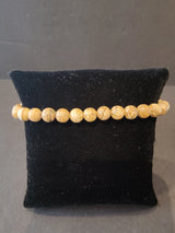 Beaded bracelet with round 6mm light brown stone beads featuring natural speckled patterns, displayed on a small black velvet pillow against a dark background.