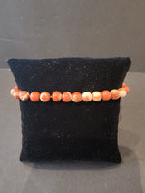 Bracelet of 6mm round orange and cream marbled stone beads displayed on a black velvet cushion with a plain gray background.