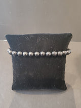 Stretch bracelet of uniformly sized polished gray stone beads about 6mm in diameter displayed on a small black fabric cushion.