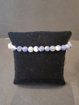 Bracelet of smooth round 6mm beads in varying shades of light blue, white, and gray displayed on a black velvet cushion.