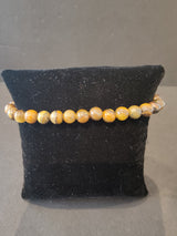 Bracelet composed of small round 6mm tiger's eye stone beads strung together and displayed on a black velvet cushion.