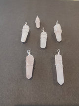 Six translucent crystal pendants wrapped in silver wire, arranged on a dark gray surface, varying slightly in size and shape with pointed ends.