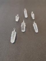 Six clear quartz crystal pendants wrapped in silver wire, arranged on a dark gray surface with varying shapes and wire styles.