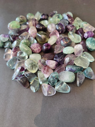 Three multi-color rainbow fluorite tumbled stones on a white background showcasing purple, green, and clear hues