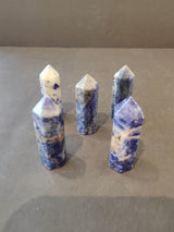 Five blue and white crystal towers with pointed tops arranged in a loose cluster on a gray surface, varying in blue intensity and white marbling.