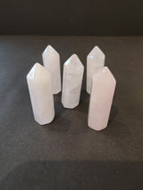 Five polished light pink to white crystal towers with hexagonal bases standing upright on a dark surface in a loose cluster.