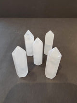 Five milky white crystal tower sculptures standing upright on a dark surface, each with a faceted pointed top and smooth polished sides.