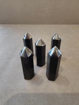 Five black hexagonal tower crystals with pointed silver metallic tops arranged on a gray surface.