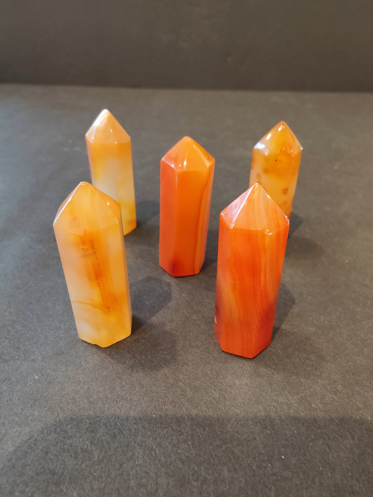 Five orange and white crystal cut tower sculptures with pointed tops arranged on a dark gray surface showing varied marbled patterns.