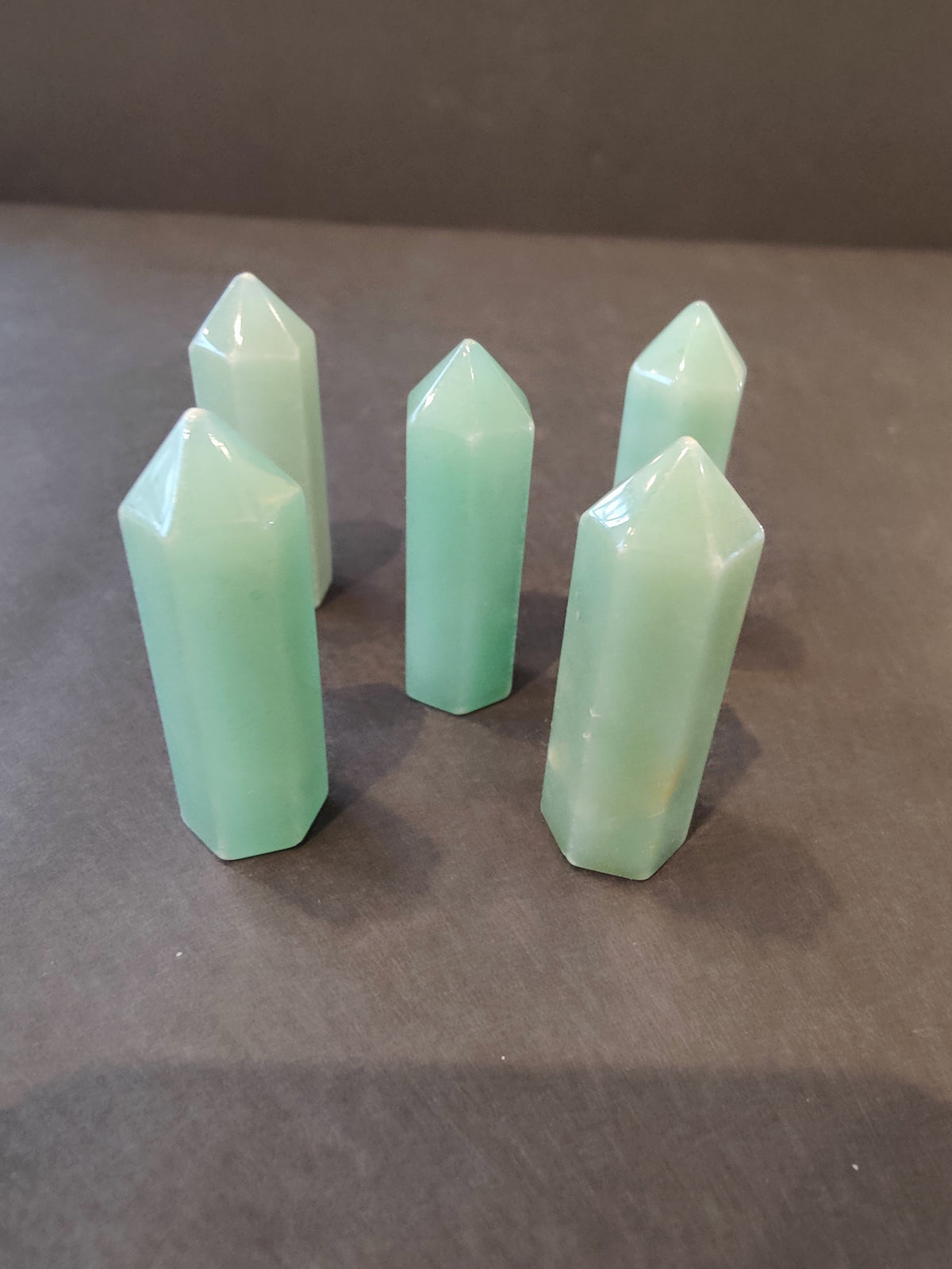 Five pale green translucent crystal towers with pointed hexagonal tops arranged on a dark brown surface, casting soft shadows.