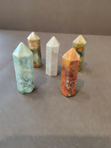 Five polished crystal towers in varied colors including blue-green, white, orange, and brown, arranged standing on a smooth gray surface.