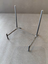 Black wrought iron display stand with a rectangular base and two vertical support rods, placed on a gray surface with a plain background.
