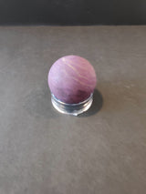 Spherical purpurite stone displaying a smooth deep purple surface with lighter striations, resting on a clear round stand against a dark background.