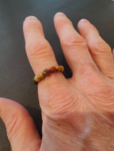 Close-up of a hand wearing a beaded stone ring with 4mm round beads in earthy tones of brown and red against a black background.