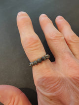 Close-up of a hand wearing a beaded ring with small, round, black and gray marbled stone beads against a dark background.