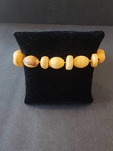 Beaded bracelet with alternating round and oval light and dark wood beads displayed on a black velvet stand against a dark background.