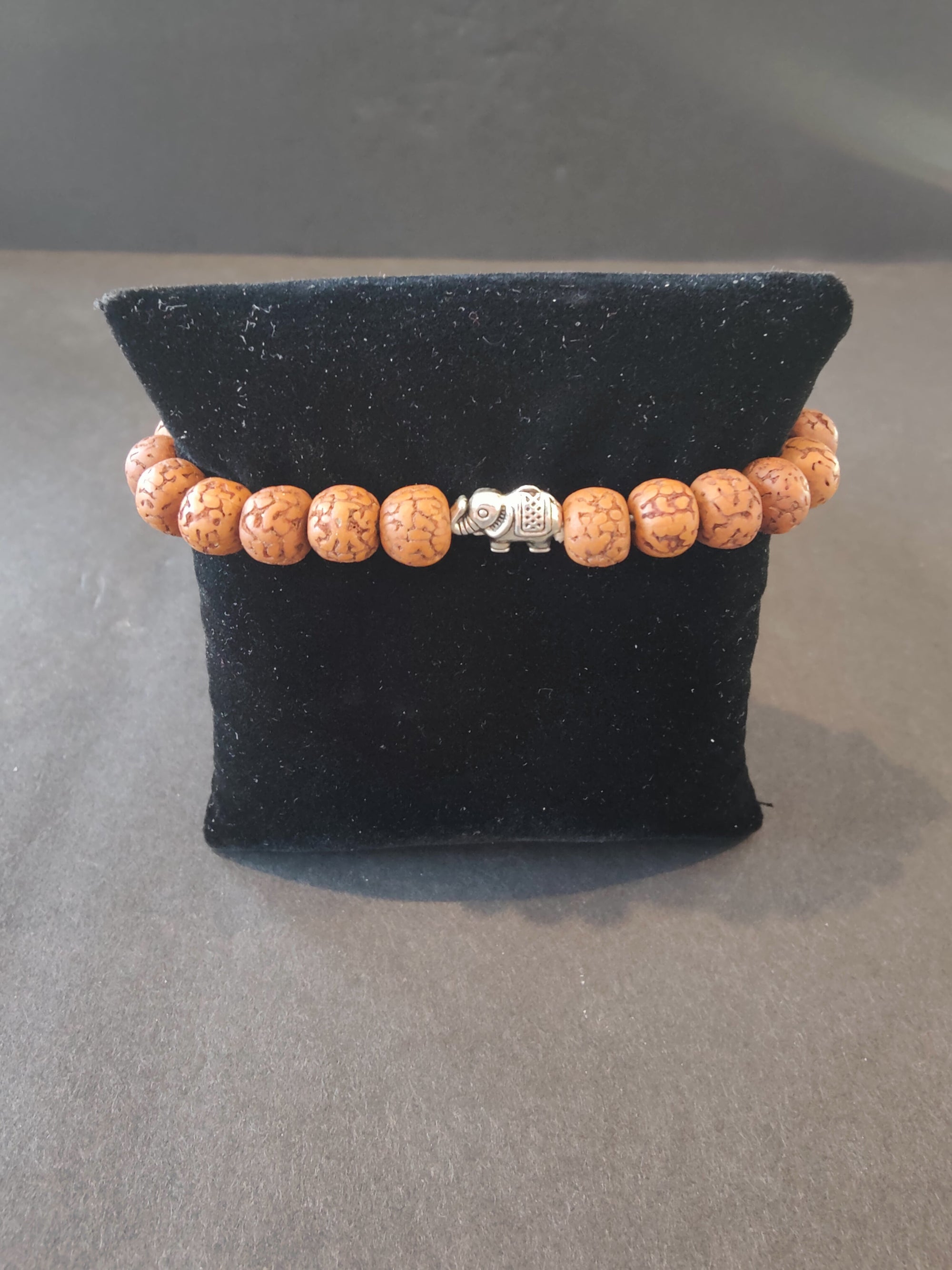 Bracelet of rudraksha seed beads with small silver elephant charms arranged on a white background