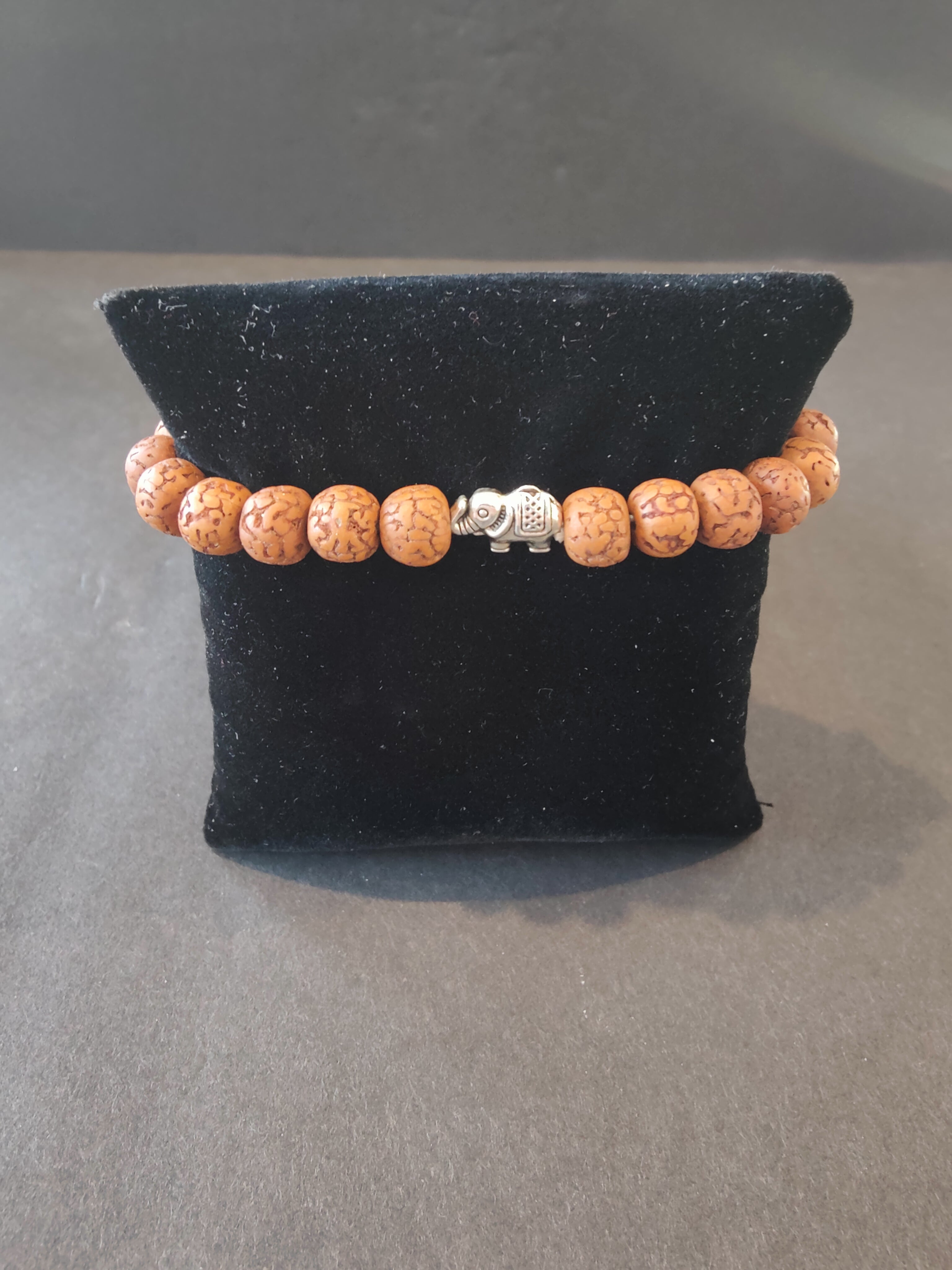 Bracelet of rudraksha seed beads with small silver elephant charms arranged on a white background