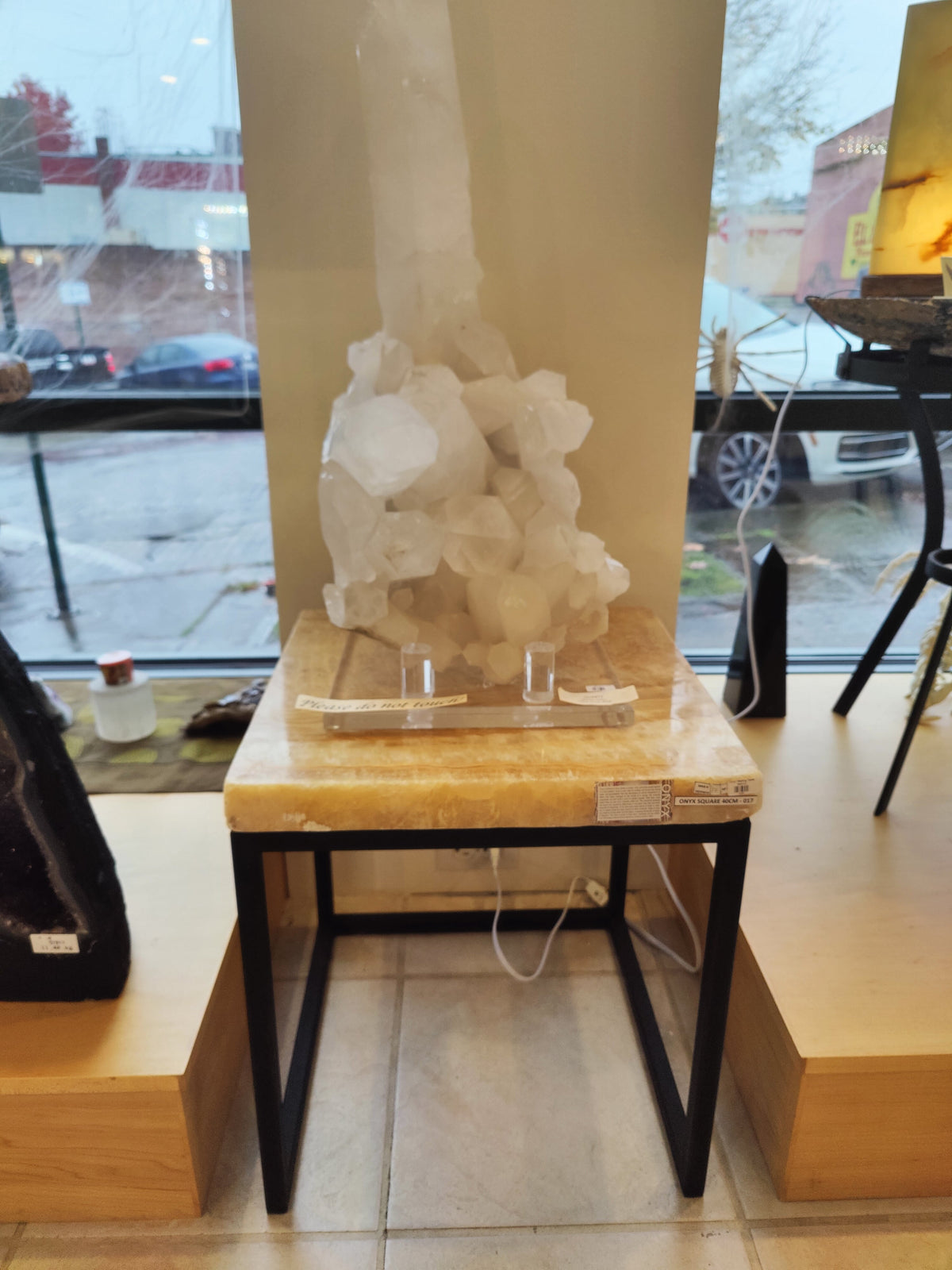 Onyx nesting table with a smooth beige stone top on black metal legs, displayed indoors against a window with parked cars visible outside.