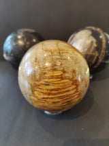Three polished spherical stones with natural patterns, featuring a central tan and brown petrified wood sphere flanked by smaller darker patterned spheres on a gray background.
