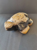 Carved turtle sculpture crafted from petrified wood with visible natural grain patterns and a polished surface, shown against a dark background.