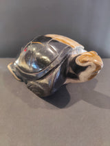 Small carved turtle sculpture made from polished petrified wood with dark brown, tan, and amber tones, showing detailed shell and head features.